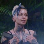 Edith Stehfest im Dschungelcamp mit Kopftuch und Tattoos am Hals, während sie inmitten des Dschungels diskutiert. Die Stimmung scheint angespannt.