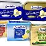 Ein Sortiment verschiedener Butterprodukte der Marke „Landfein“ in unterschiedlichen Verpackungen. Oben sind zwei blaue Plastikdosen „Die Streichbare“ zu sehen – eine mit Alpensalz, die andere ungesalzen. Darunter befinden sich drei Butterstücke in Papierverpackung: „Deutsche Süßrahmbutter“ in goldener Verpackung, „Deutsche Markenbutter“ in blauer Verpackung und „Original Irische Butter“ in goldener Verpackung mit grünem Aufdruck und einer Kuhillustration.