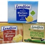 "Drei verschiedene Butterprodukte der Marke Landfein, gestapelt aufeinander. Oben: Eine Packung 'Deutsche Markenbutter' in blauer Verpackung, mild gesäuert und ohne Gentechnik. Unten links: Eine Packung 'Deutsche Süßrahm Butter' in gelb-roter Verpackung mit dem Zusatz 'sahnig-frisch'. Unten rechts: Eine Packung 'Original Irische Butter' in goldener Verpackung mit einer Kuh und Kleeblatt-Symbolen, als 'streichzart' gekennzeichnet.