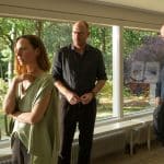 "Wendland - Stiller und der Teufelssauger": Jakob Stiller (Ulrich Noethen), Oda Nolde (Katharina Schüttler) und Jan Nolde (Johann von Bülow) stehen zusammen in einem Wohnzimmer. Oda Nolde steht mit dem Rücken zu Jakob Stiller und Jan Nolde. Hinter ihnen ist der Garten durch eine Fensterfront zu sehen.