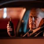 "Die Spur des Killers – Midnight in the Switchgrass": FBI-Agent Karl Helter (Bruce Willis) sitzt nachts in einem Auto und schaut durch das offene Fahrerfenster nach draußen. In der Hand hält er ein Funkgerät.