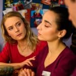 "Bettys Diagnose - Verfahren": Mia (Antonia Döring) und Lukas (Niklas Löffler) beobachten Ava (Rona Özkan), die mit geschlossenen Augen zwischen ihnen sitzt. Neben Mia steht ein rosafarbenes Sparschwein auf einem Tresen. Im Hintergrund hängt eine Pinnwand mit verschiedenen Bildern.