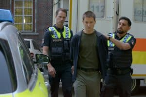 "Notruf Hafenkante - Der Preis der Lüge": Der Polizist Malik (Zejhun Demirov) führt Jul (Juri Winkler) in Richtung eines Streifenwagens. Juls Hände sind auf dem Rücken fixiert. Neben Jul läuft der Polizist Mattes Seeler (Matthias Schloo). Er schaut nachdenklich.