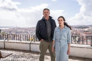 "Flucht aus Lissabon": Sophia (Hana Sofia Lopes) steht zusammen mit Tom Fährmann (Hans Sigl) auf einer bekannten Aussichtsplattform in Lissabon. Mit ernster und fragender Miene schauen beide in Richtung Kamera. Tom Fährmann hat die Hände in den Hosentaschen. Im Hintergrund sieht man die Häuser der Stadt von oben.