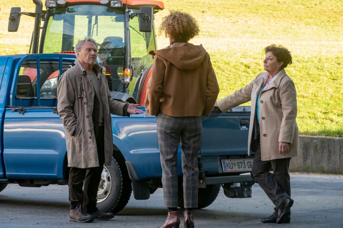 "Der Bergdoktor: Herzschmerzen": Auf dem Hof des Landhandels: Lisbeth Gruber (Monika Baumgartner) steht neben ihrem Pickup und beobachtet aufmerksam ein Gespräch zwischen Rolf Pflüger (Wolfram Berger) und seiner Tochter Caro Pflüger (Barbara Lanz).
