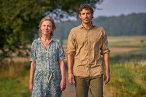 "Zimmer im Grünen - Herzenswege": Frieda (Therese Hämer) und Heinrich (Tobias van Dieken) laufen entspannt auf einem von Wiesen umgebenen Weg, im Hintergrund liegt der Waldrand.