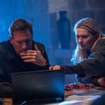 "Geheimsache Malta": MI6-Analystin Kacey (Abigail Breslin) zeigt Auftragskiller Shaw (Aaron Eckhart) etwas auf dem Laptop. Auf dem Tisch, an dem sie sitzen, liegen verschiedene Schraubenzieher und Kabel, der Hintergrund ist in blaues Licht getaucht.
