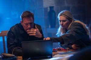 "Geheimsache Malta": MI6-Analystin Kacey (Abigail Breslin) zeigt Auftragskiller Shaw (Aaron Eckhart) etwas auf dem Laptop. Auf dem Tisch, an dem sie sitzen, liegen verschiedene Schraubenzieher und Kabel, der Hintergrund ist in blaues Licht getaucht.
