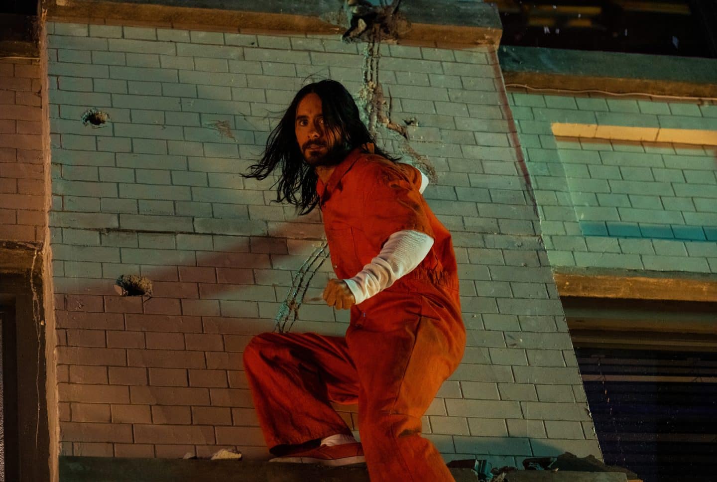 "Morbius": Dr. Michael Morbius (Jared Leto) trägt einen orangen Overall und klettert mit angespannter Körperhaltung an einer Wand hinunter.
