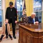 "Trump und seine Milliardäre": Trump sitzt an seinem Schreibtisch im Oval Office des Weißen Hauses und spricht mit Elon Musks Sohn. Elon Musk steht lachend hinter dem Jungen, der breitbeinig posiert.