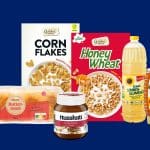 Produktauswahl der ALDI-Preissenkung 2025: Golden Bridge Cornflakes, Golden Bridge Honey Wheat, Bellasan Sonnenblumenöl, Goldähren Buttertoast, Nusskati Nuss-Nougat-Creme und Goldland Honig im Spender – vor blauem Hintergrund.