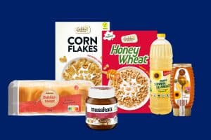 Produktauswahl der ALDI-Preissenkung 2025: Golden Bridge Cornflakes, Golden Bridge Honey Wheat, Bellasan Sonnenblumenöl, Goldähren Buttertoast, Nusskati Nuss-Nougat-Creme und Goldland Honig im Spender – vor blauem Hintergrund.