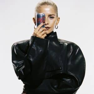 Eine Frau in schwarzer Lederjacke hält eine Coca-Cola-Light-Dose im ikonischen silbernen Design vor ihr Gesicht, wobei ein Auge sichtbar bleibt.