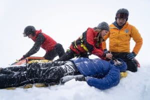 "Die Bergretter: Eiskalte Wahrheit (2)": Simon (Ferdinand Seebacher), Katharina (Luise Bähr) und Markus (Sebastian Ströbel) verarzten den verletzten Daniel Faltermayer (Julian Felix), der im Schnee liegt.