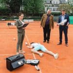 "Die Rosenheim-Cops - Alles hat ein Ende": Pathologin Atay (Sevda Polat), Kommissar Stadler (Dieter Fischer) und Kommissar Hansen (Igor Jeftić) stehen um das Mordopfer herum, das bäuchlings auf dem Tennisplatz liegt. Kommissar Hansen hält einen in transparente Folie verpackten Tennisschläger in der Hand.