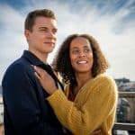"Inga Lindström: Geliebter Feind": Elli (Pia Amofa-Antwi) und Lucas (Gerrit Klein) stehen aneinander gelehnt auf der Dachterrasse der "Berginvest"-Niederlassung in Stockholm. Im Hintergrund strahlend blauer Himmel mit Wolken, Elli hat ihre linke Hand auf Lucas' Brust gelegt. Beide schauen rechts an der Kamera vorbei in die Ferne.