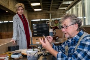 "SOKO Stuttgart – Letztes Kapitel": Klaus Michael Stoirer (Martin Semmelrogge) sitzt in der Bücherei an einem Schreibtisch, während er in der einen Hand einen Käfer und in der anderen eine Pinzette hält. Er schaut den Käfer fasziniert und konzentriert an, während sich Hauptkommissarin Martina Seiffert (Astrid M. Fünderich) an das Büchereigeländer lehnt und den Hobby-Käferspezialisten bei seiner Arbeit beobachtet.