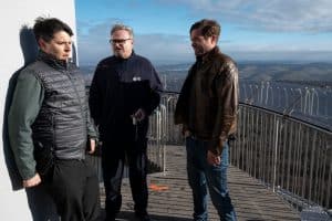 "SOKO Stuttgart – Tod im Turm": IT-Spezialist Rico Sander (Benjamin Strecker) steht mit geballten Fäusten und dem Rücken an den Turm gepresst auf der Aussichtsplattform des Stuttgarter Fernsehturms. Neben ihm befindet sich der Aufzugsführer Jürgen Spengler (Oliver Breite) und Jo Stoll (Peter Ketnath), der sich sichtlich über die Höhenangst seines Kollegen amüsiert. Im Hintergrund erstreckt sich ein Landschaftspanorama.