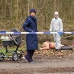 "Der Alte - Zwischenstation": Annabell Lorenz (Stephanie Stumph) steht auf einem Waldweg, hinter einem Absperrband an einem Kinderwagen und schaut sich um. Im Hintergrund liegt die Tote Marlies Thalmaier (Isabella Surel). Dr. Luisa Geiger (Sidonie von Krosigk) steht neben der Leiche und sieht Richtung Annabell Lorenz.