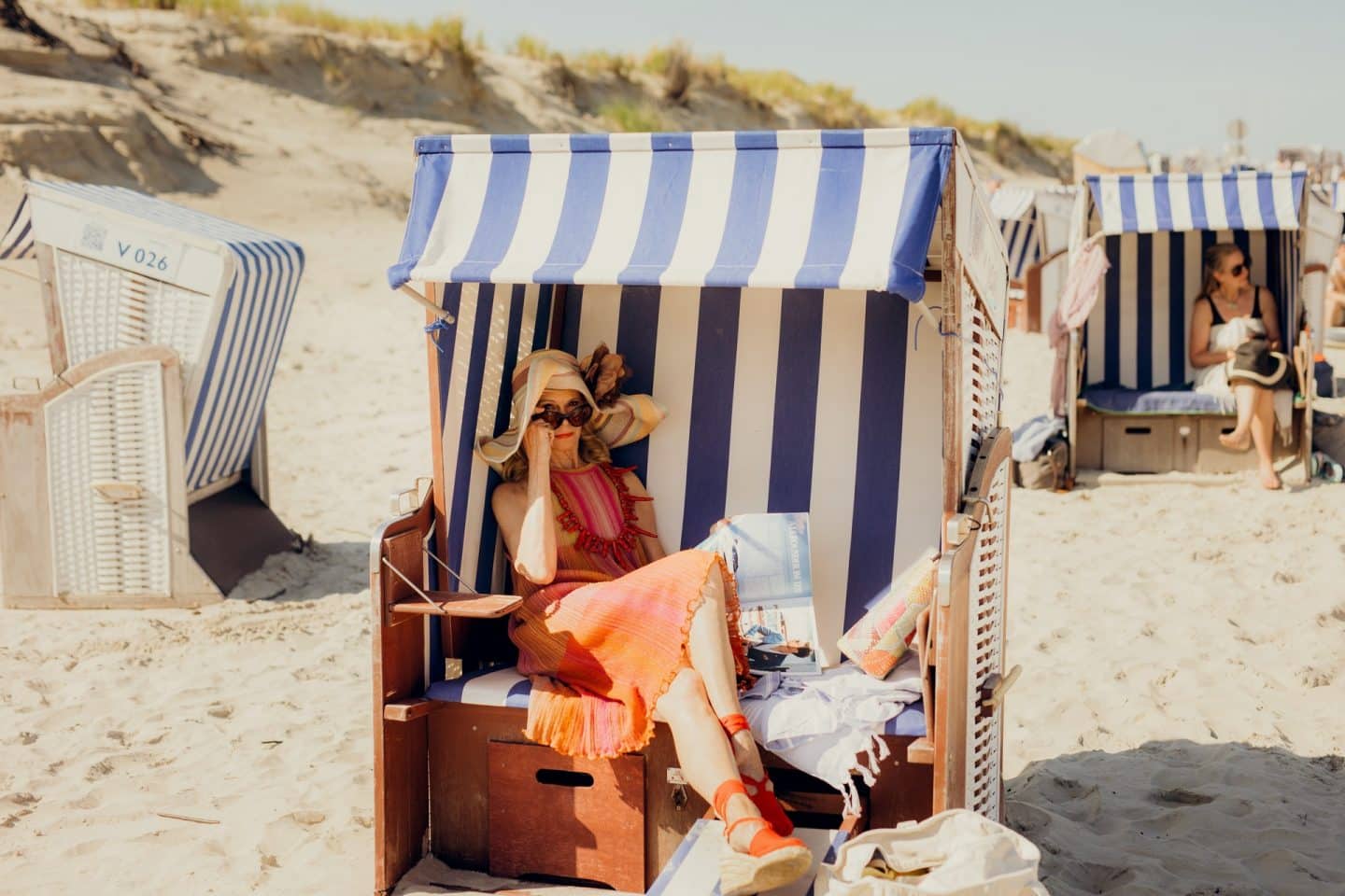 "Verhängnisvolle Leidenschaft Sylt": Lust, Lügen, Leidenschaft – so heiß wird das Herzkino heute! 2 "Verhängnisvolle Leidenschaft Sylt": Am Stand: Hedi von Carlsberg (Leslie Malton) sitzt in einem Strandkorb. Sie hat die Beine übereinandergeschlagen und blickt, die Sonnenbrille leicht heruntergezogen, keck in die Kamera.