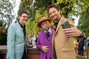 "Bares für Rares - Deutschlands größte Trödelshow": Colmar Schulte-Goltz, Horst Lichter und August Wittgenstein stehen dicht nebeneinander am Expertisenpult und lachen in Wittgensteins Handy, das dieser zum Selfie ausgestreckt in der linken Hand hält. Im Hintergrund steht das Publikum vor Bäumen.