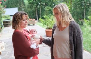 "Lena Lorenz - Das halbe Lottchen": Auf einer Terrasse stehen sich Lena Lorenz (Judith Hoersch) und Magali Bernbauer (Hanna Plaß) gegenüber. Magali hält mit traurigem Gesichtsausdruck ein Baby im Arm. Lena schaut sie mitfühlend an und legt tröstend ihre Hand auf Magalis Arm.