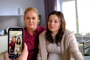 "Lena Lorenz - Vor aller Augen": In einem Krankenzimmer sitzen Lena Lorenz (Judith Hoersch) und Nadja Brettschneider (Vivien König) nebeneinander auf einem Bett. Beide schauen in eine Handykamera, die auf sie gerichtet wird.