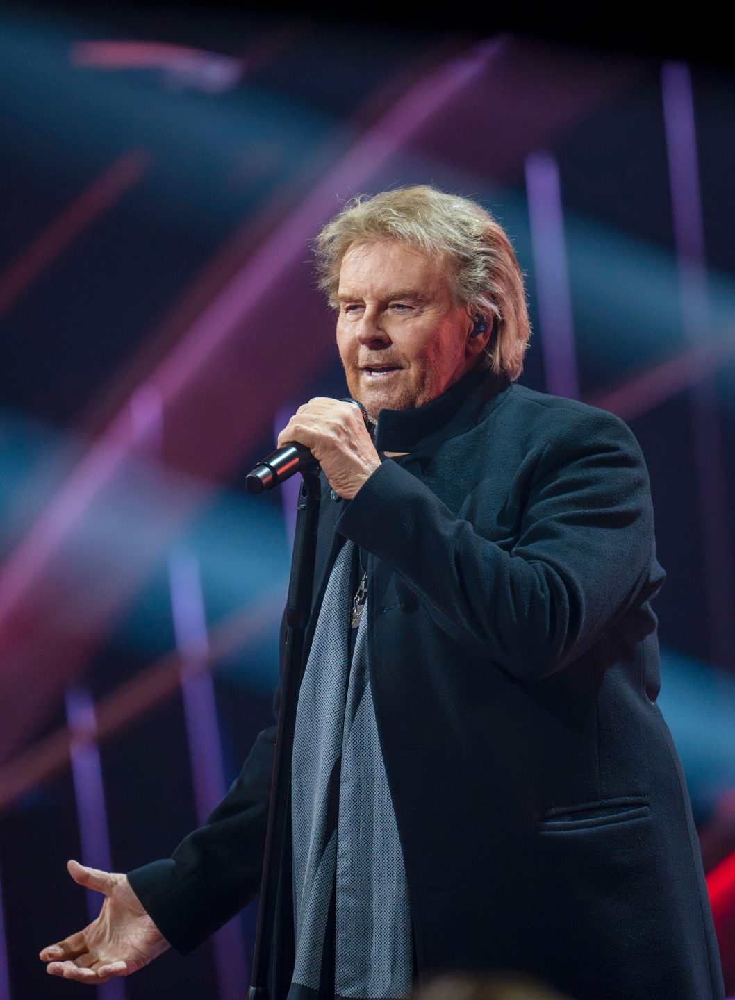 "Die Giovanni Zarrella Show": Howard Carpendale steht auf der Bühne und singt in ein Mikrofon. Er trägt eine schwarze, lang geschnittene Jacke sowie einen grauen Schal. Der Hintergrund ist in dunklen Tönen gehalten und mit diagonalen, lilafarbenen Lichtstreifen durchzogen.
