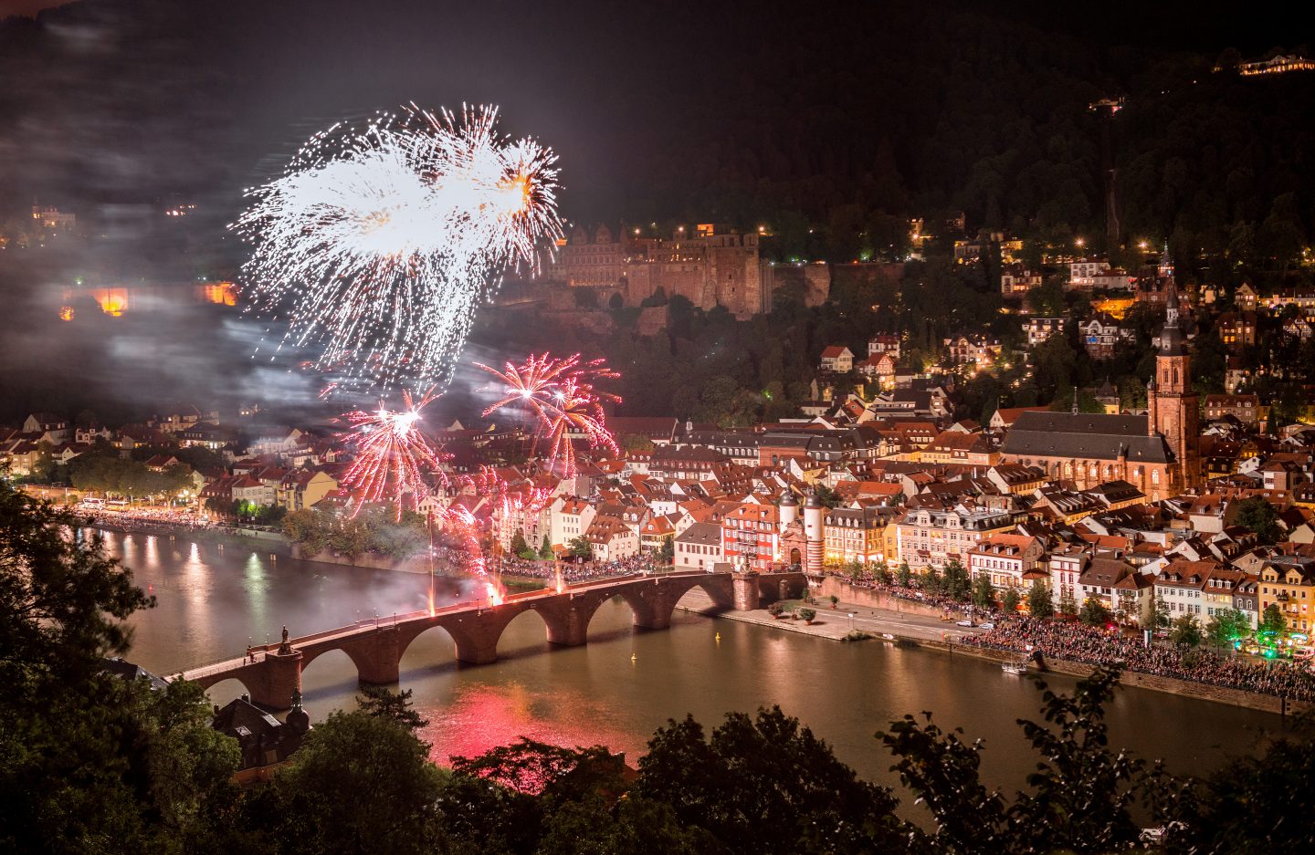 Feuerwerk über der Heidelberger Altstadt bei Nacht, mit der beleuchteten Alten Brücke und dem Heidelberger Schloss im Hintergrund.