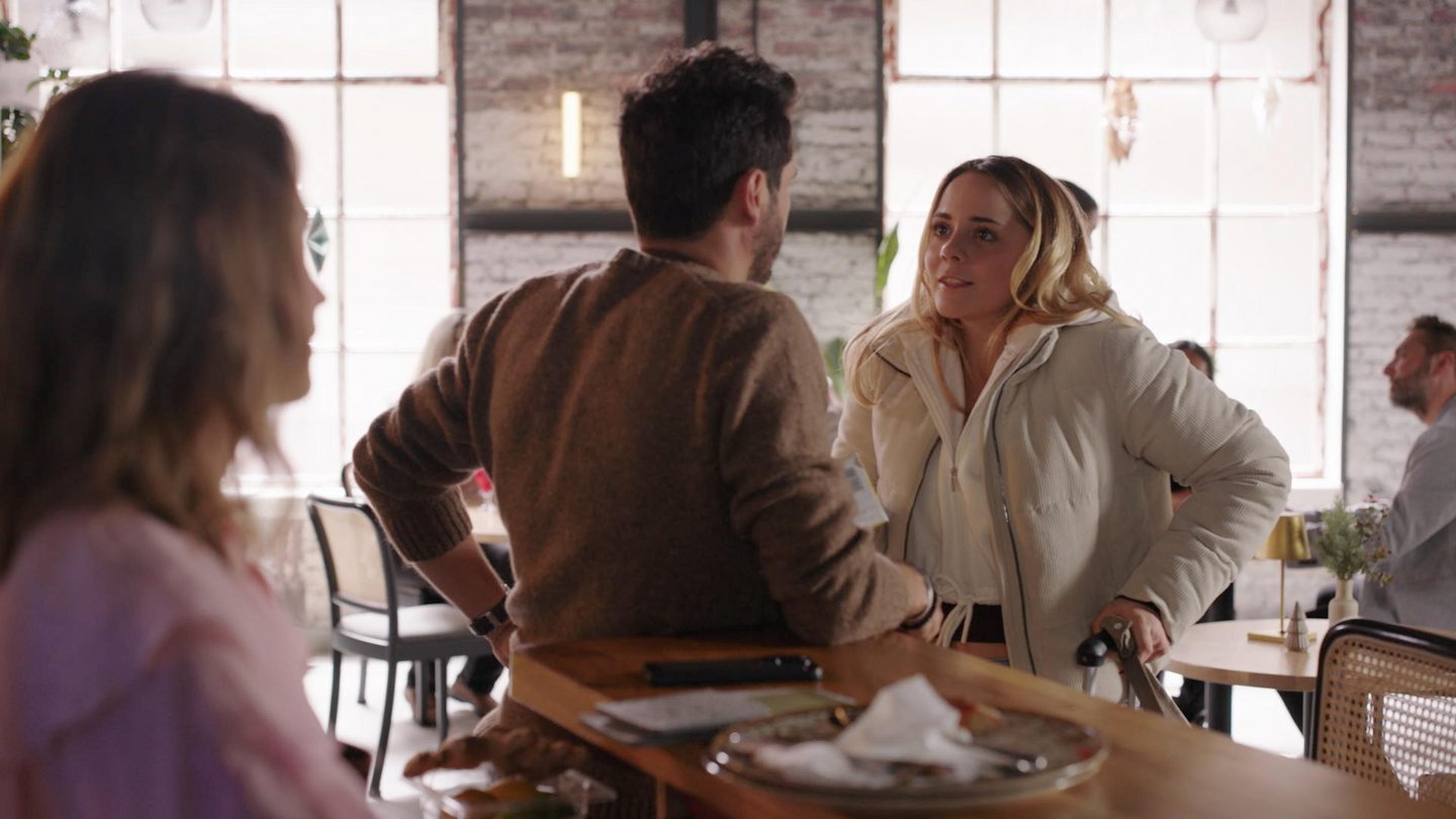Nathalie, Matteo und Valea stehen gemeinsam in einem Café und führen ein angespanntes Gespräch, während Nathalie zwischen den beiden Männern positioniert ist.