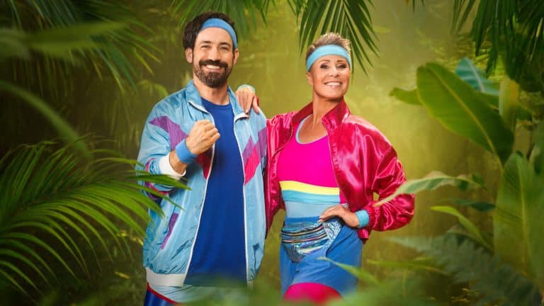 Die Moderatoren Jan Köppen und Sonja Zietlow in bunter 80er-Jahre-Sportkleidung vor einem Dschungelhintergrund mit dem Logo „Ich bin ein Star – Holt mich hier raus!“.