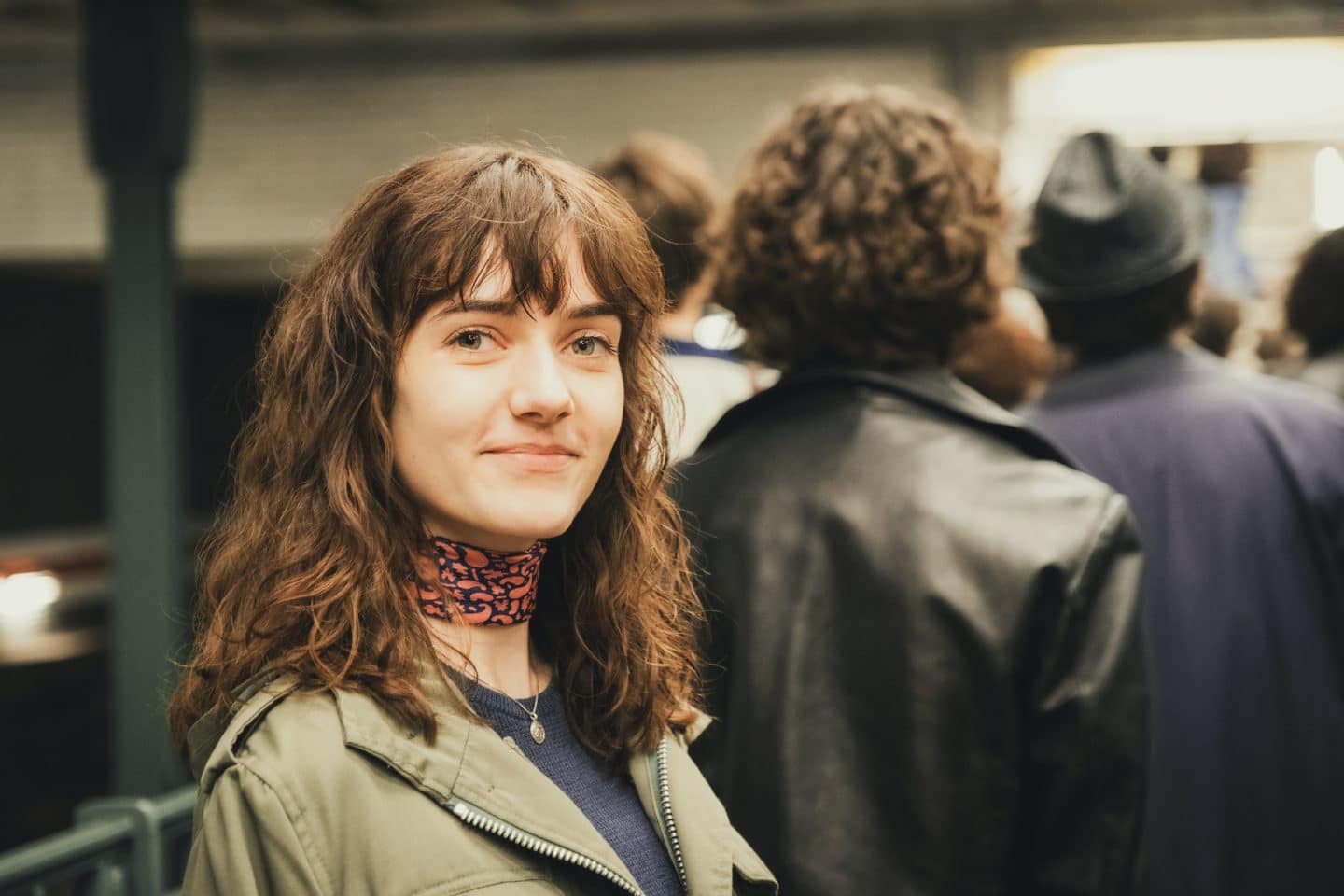 "Ku'damm 77": Friederike von Boost (Marie Louise Albertine Becker) steht an einer U-Bahn-Station und sieht lächelnd in die Kamera.