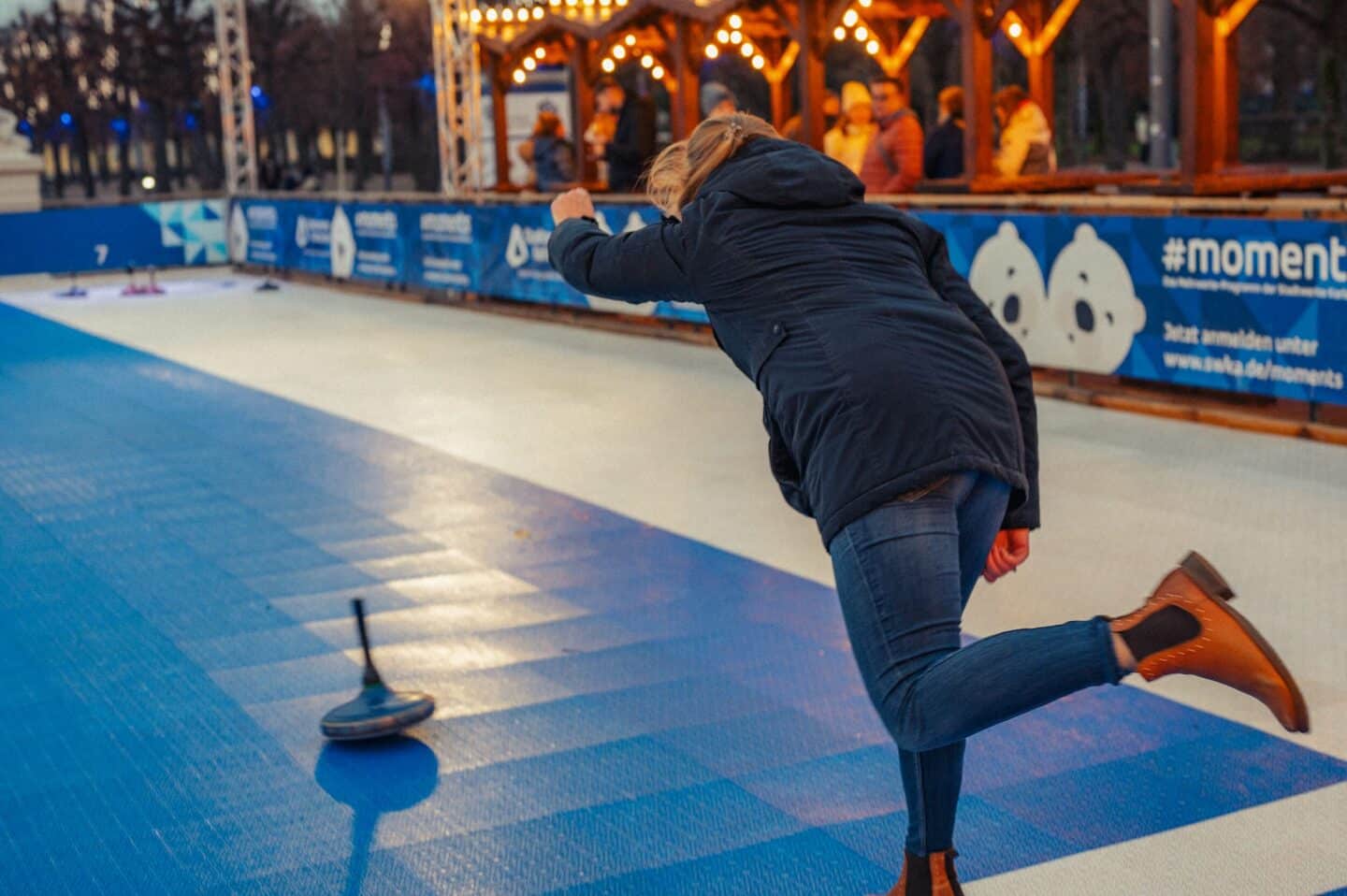 Eine Person spielt Curling auf einer blauen Eisbahn.