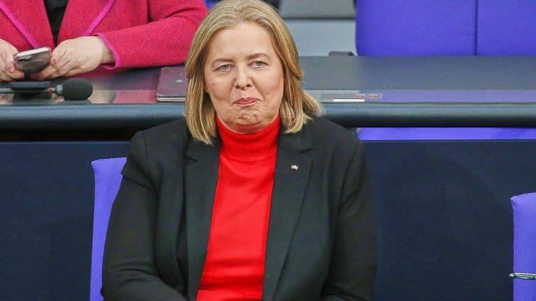 Frau mit blonden Haaren in rotem Oberteil und schwarzem Blazer sitzt im Parlament.