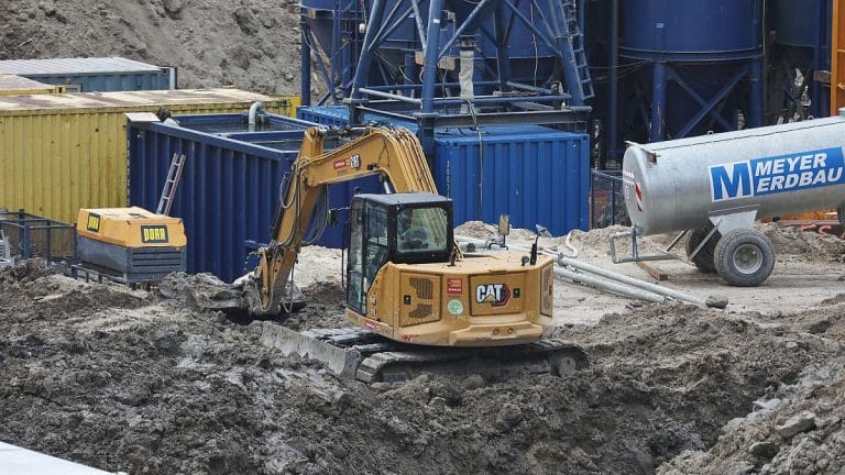 Bagger auf einer Baustelle mit Containern im Hintergrund.