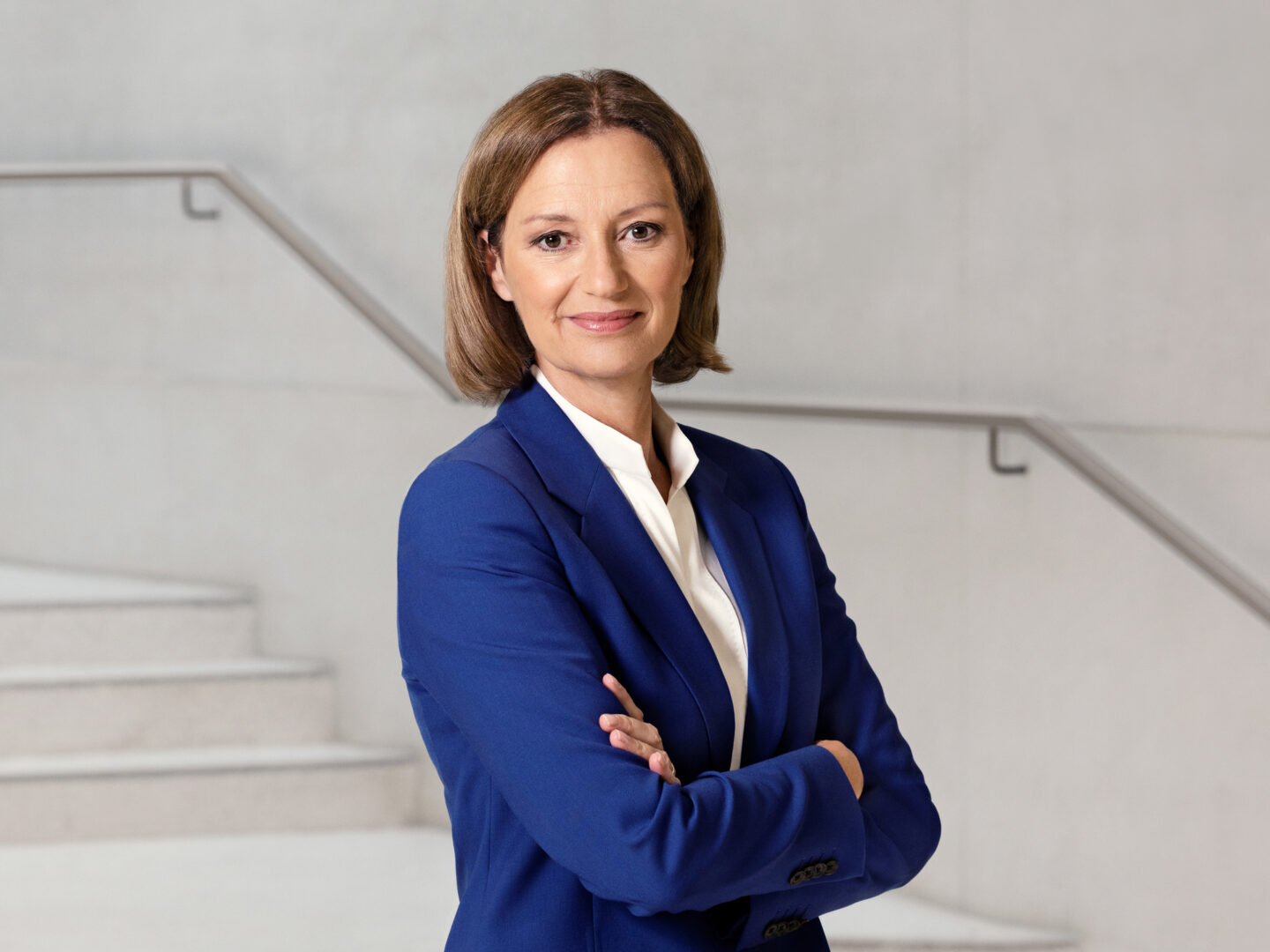 Frau in blauer Blazerjacke steht mit verschränkten Armen.