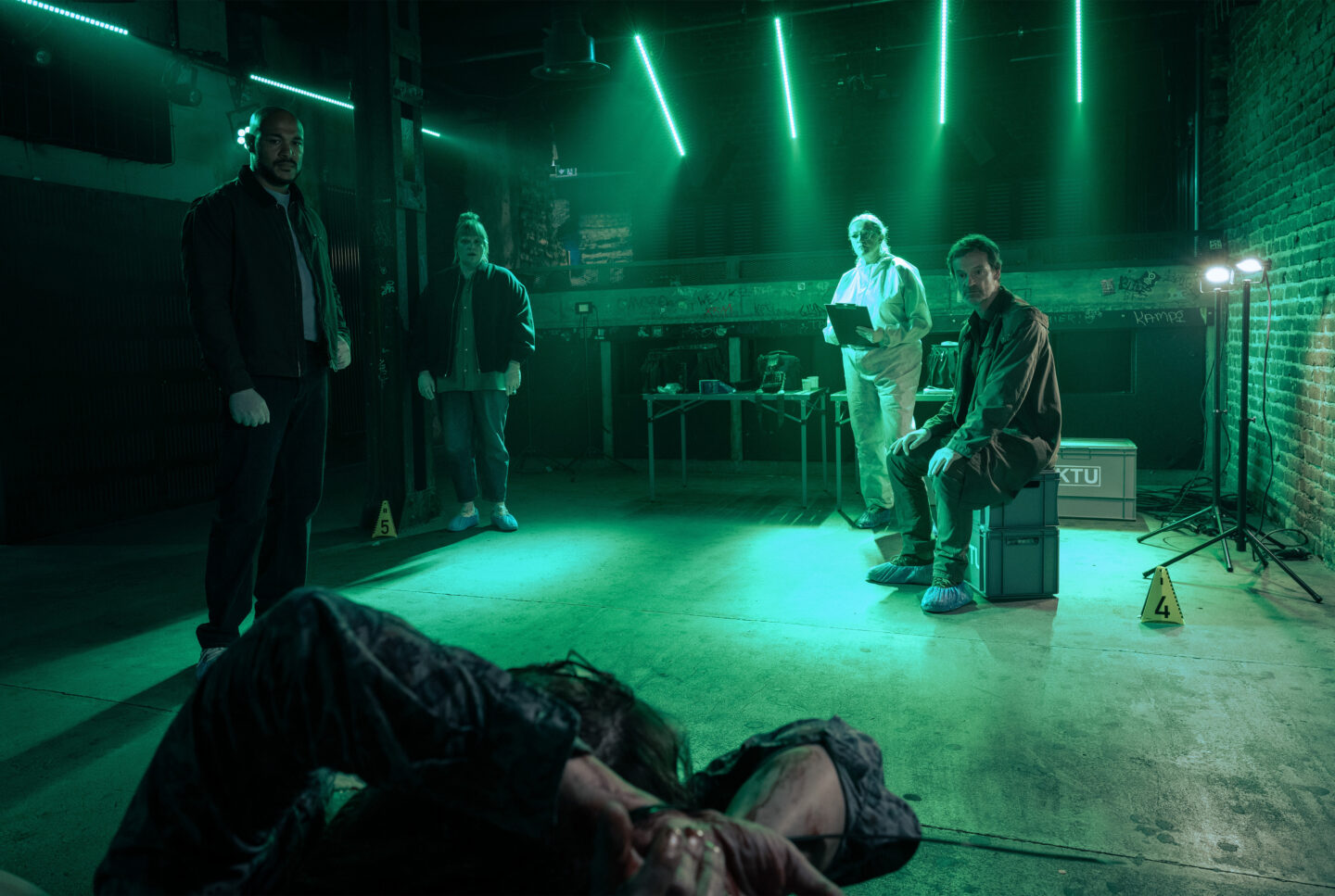 Szenario mit vier Personen in einem dunklen Raum, eine Person liegt am Boden.