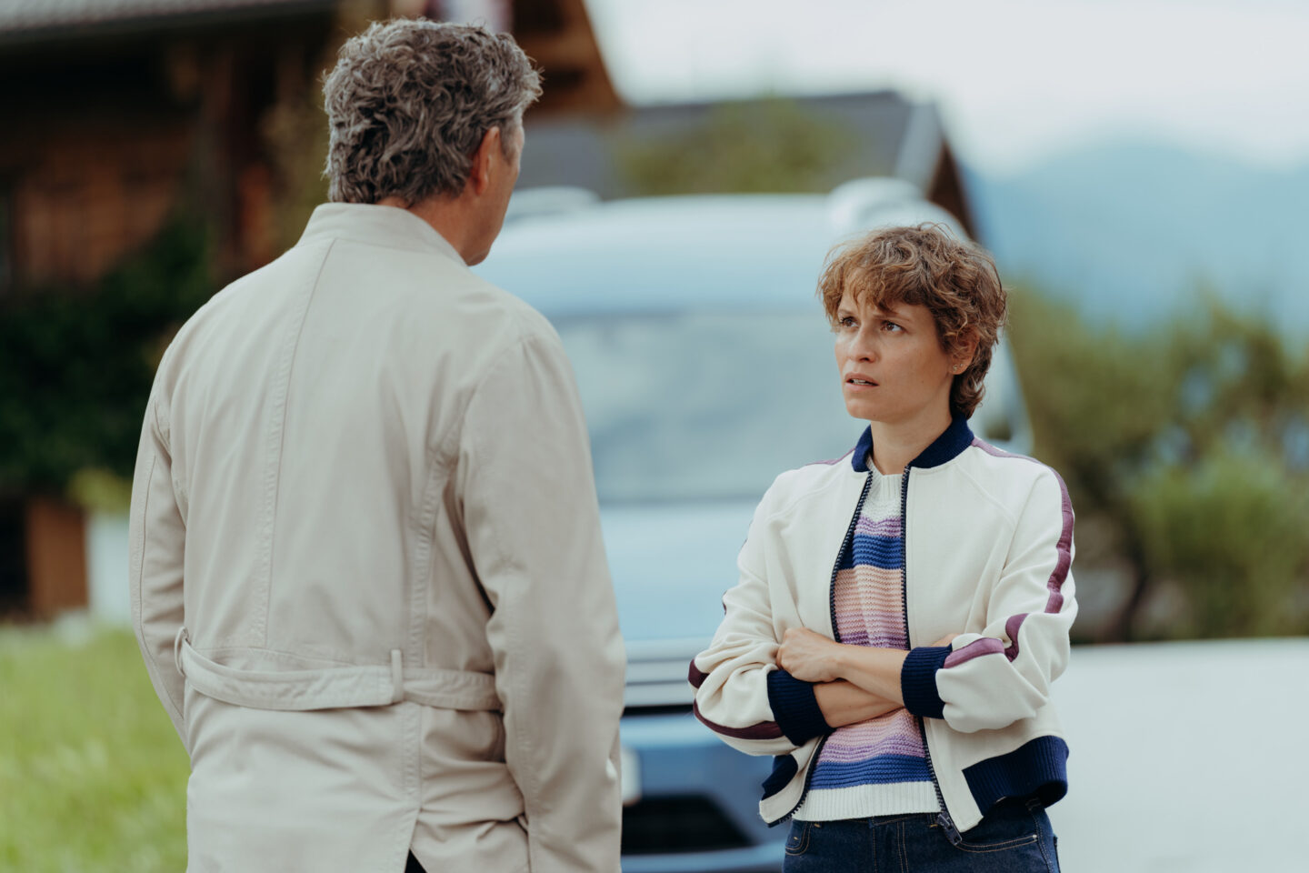 Mann und Frau im Gespräch, im Hintergrund ein Fahrzeug und ländliche Umgebung.