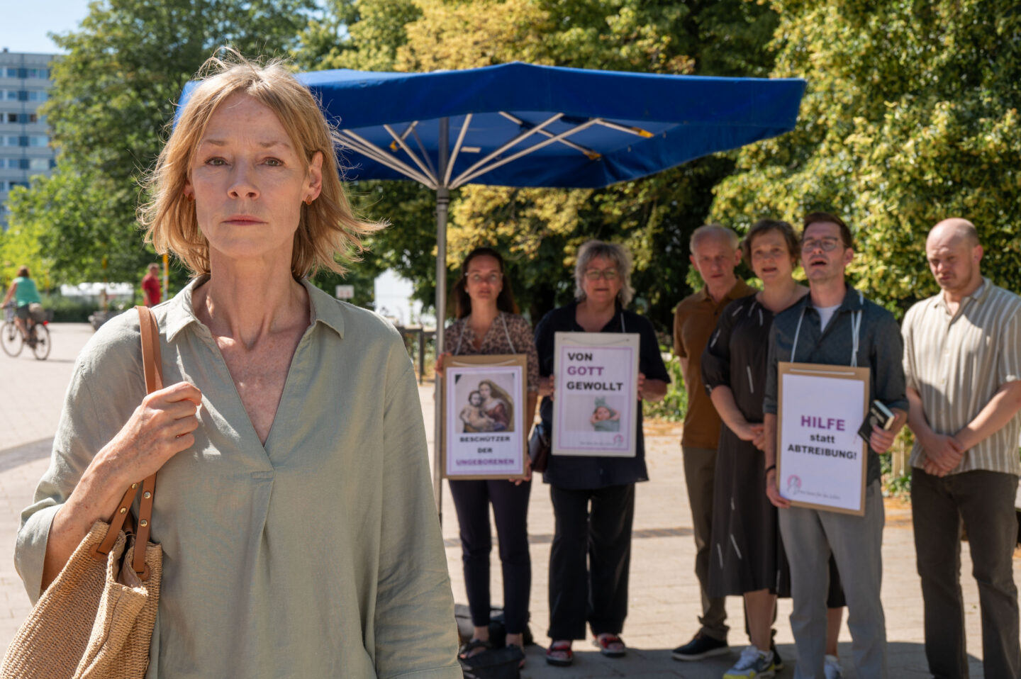 Frau steht im Vordergrund, im Hintergrund Gruppe mit Plakaten.