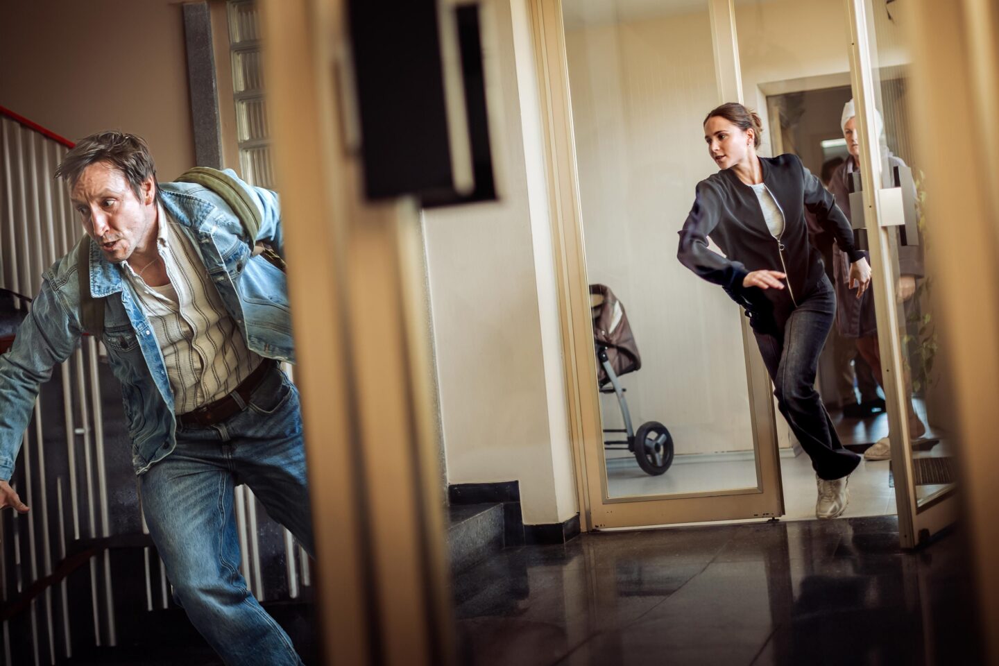 Mann in Jeansjacke flieht, während eine Frau in sportlicher Kleidung ihm folgt.