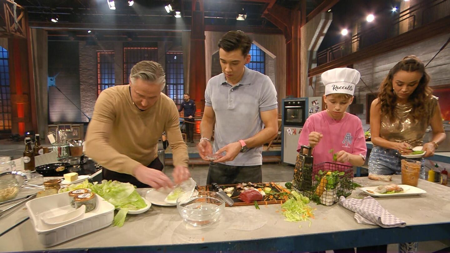 Vier Personen kochen in einer modernen Küche, Zutaten auf dem Tisch.