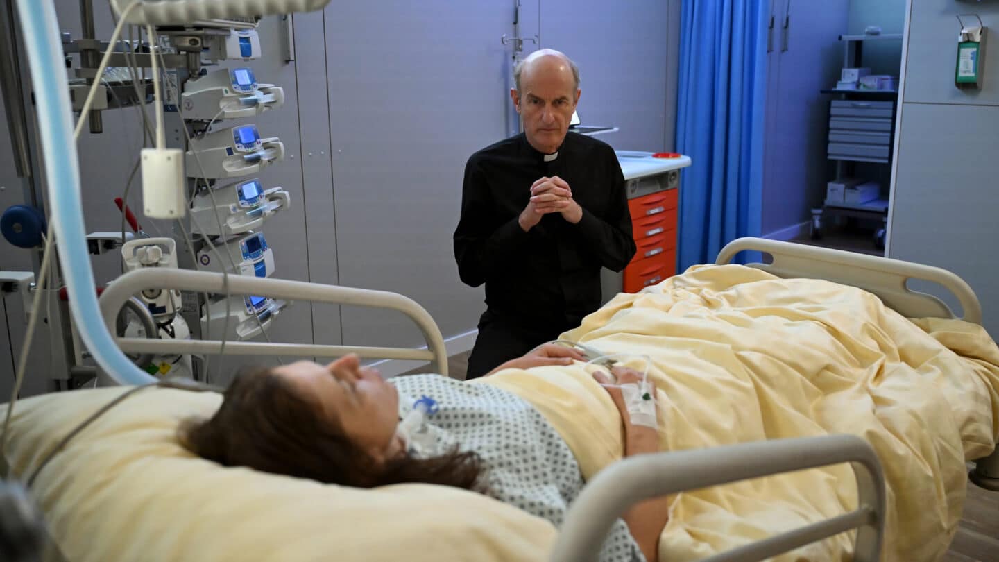 Ein Priester betet am Bett einer kranken Person im Krankenhaus.
