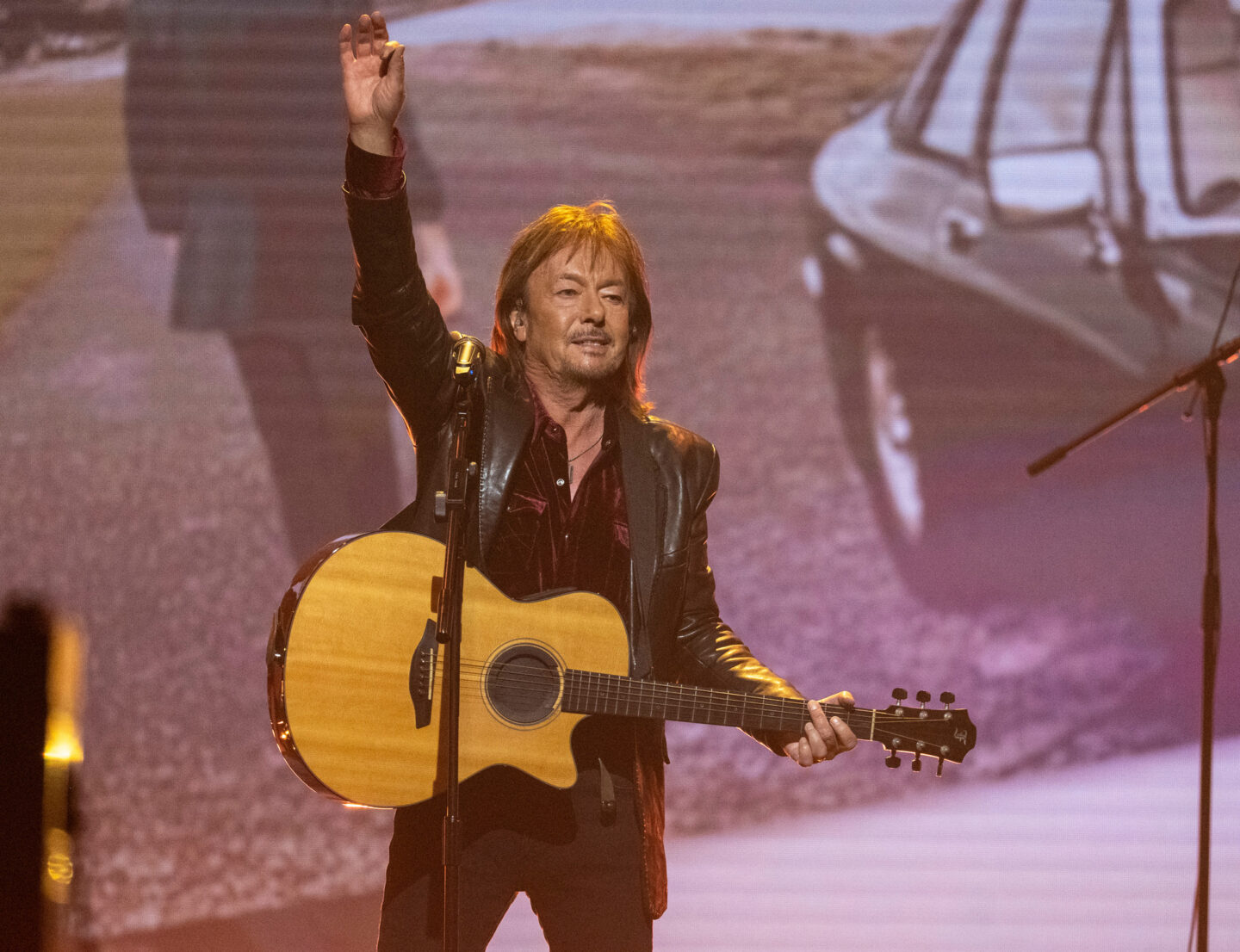Mann mit Gitarre auf der Bühne, hebt die Hand zum Gruß.