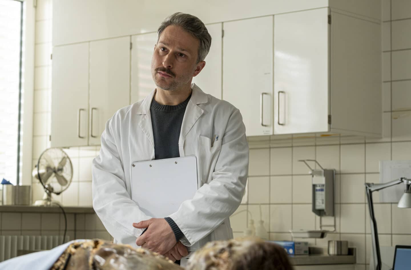 Mann in weißem Kittel steht in einem Untersuchungsraum.