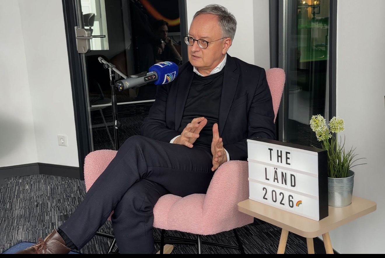 Mann im Anzug sitzt in einem modernen Raum und spricht in ein Mikrofon.