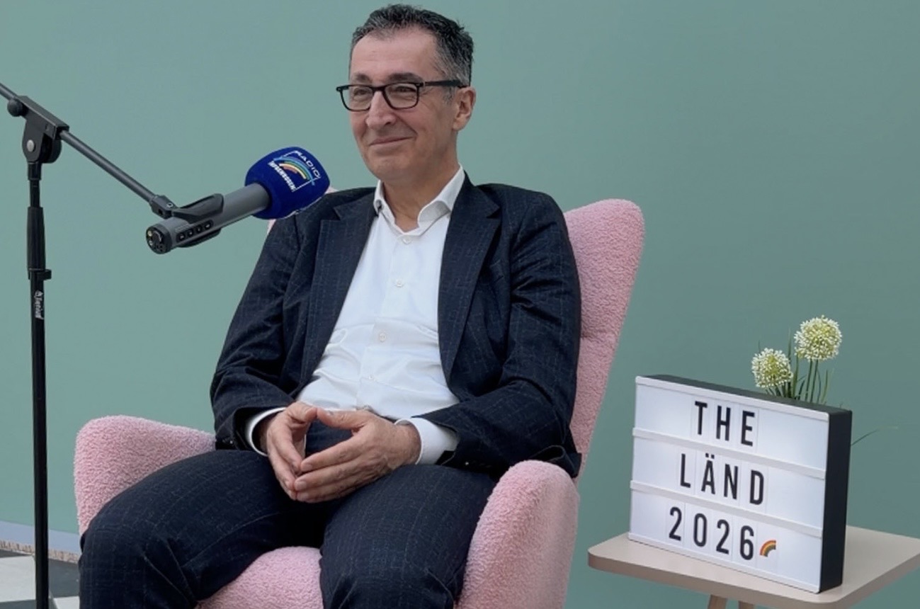 Mann im Anzug sitzt auf einem pinken Sessel mit Mikrofon und Lichtbox.