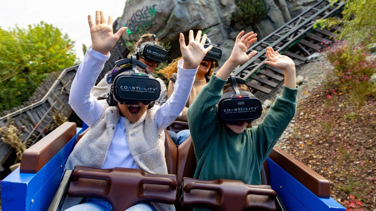 Zwei begeisterte Kinder mit VR-Brillen erleben eine Achterbahnfahrt im Europa-Park. Mit erhobenen Armen genießen sie das virtuelle Coastiality-Erlebnis, während die Schienen und die Felslandschaft im Hintergrund die immersive Kombination aus realer und digitaler Welt unterstreichen.