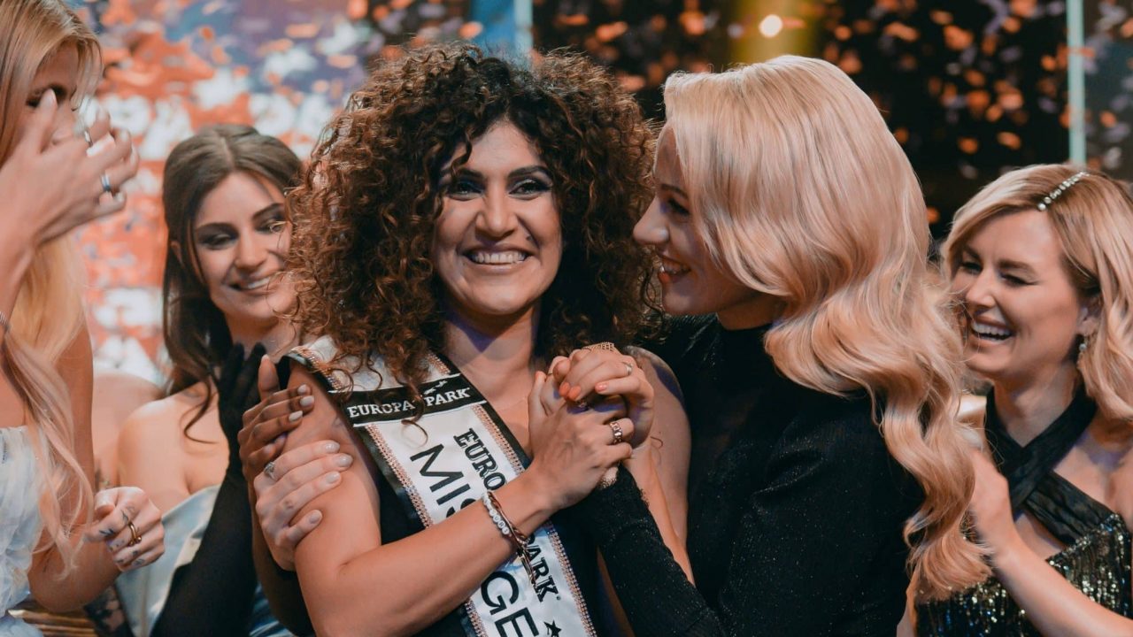 Apameh Schönauer, die Gewinnerin von Miss Germany 2024, wird von Mitfinalistinnen und Moderatorin Lola Weippert umringt und gefeiert. Die Szene zeigt die emotionale Krönung der Siegerin auf der Bühne des Europa-Parks Rust, begleitet von Konfetti und jubelnden Teilnehmerinnen.