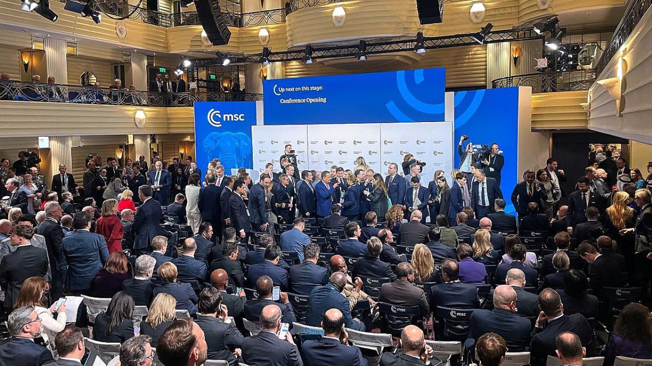 Menschenmenge bei einer Konferenz mit einem großen Bildschirm im Hintergrund.